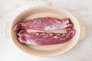 Raw pork tenderloins seasoned with salt and pepper in a baking dish before roasting.