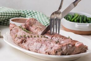 Cooked pork tenderloins resting on a platter while being sliced into medallions.