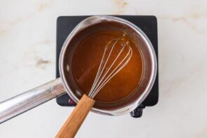 Sweet citrus glaze simmering in a saucepan and being whisked until smooth and glossy.