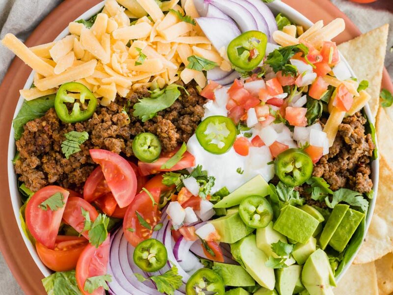 a bowl filled with taco ingredients for a salad - ground beef, cheese, pico de gallo, avocado