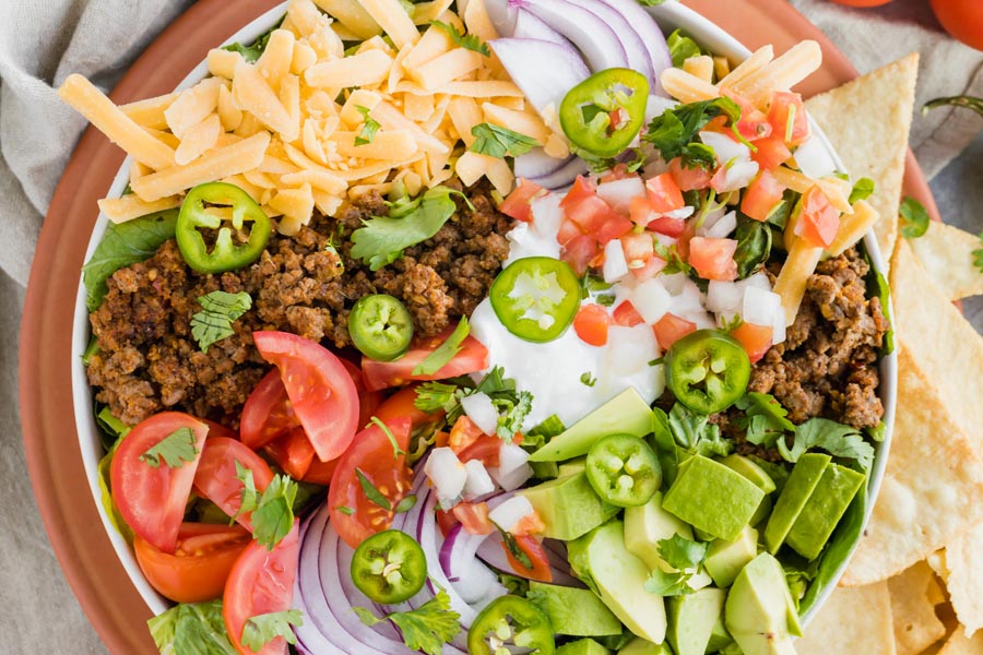 a bowl filled with taco ingredients for a salad - ground beef, cheese, pico de gallo, avocado