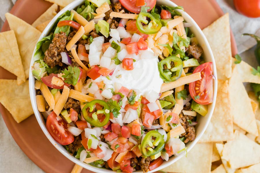a top down view of a taco salad topped with slice jalapeno and chips beside it