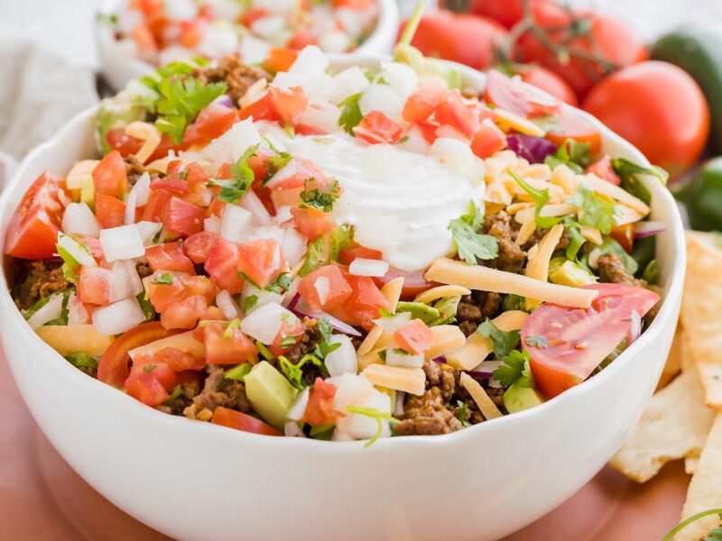 a taco salad topped with sour cream and pico de gallo in a white bowl