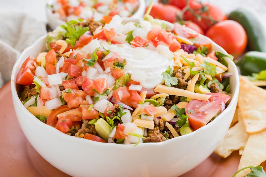 a taco salad topped with sour cream and pico de gallo in a white bowl