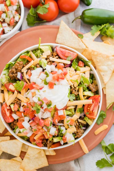 a bowl of salad next to tortilla chips, tomatoes and jalapenos