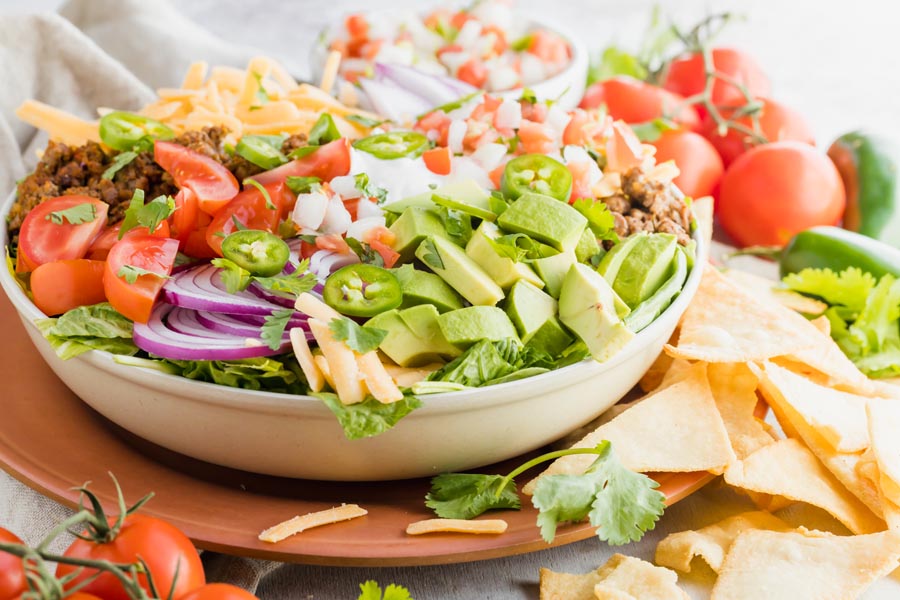 a salad with red onion, avocado, jalapeno chips and tomatoes sits in from of corn chips