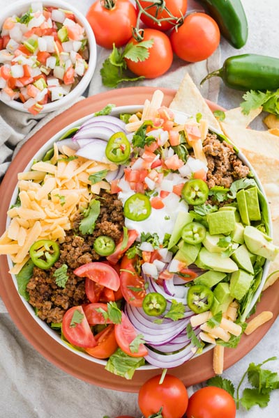 a healthy taco salad on an orange plate with salsa ingredients around