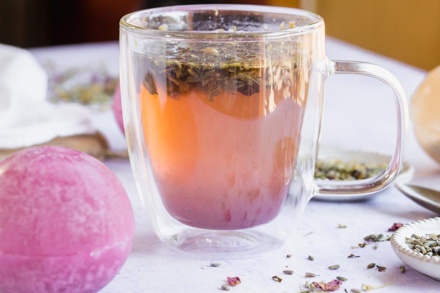 a clear mug of purple tea with loose flower leaves inside
