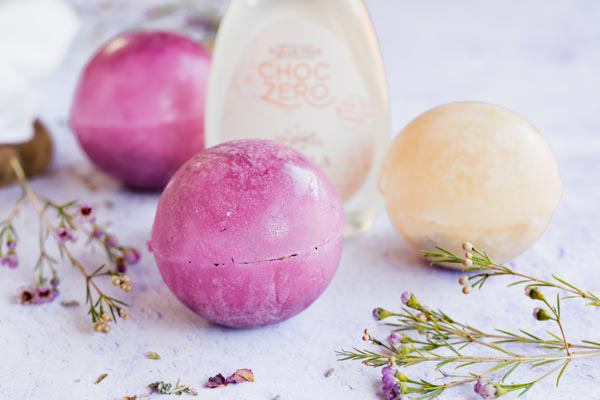 three colorful tea bombs next to flowers and a syrup bottle