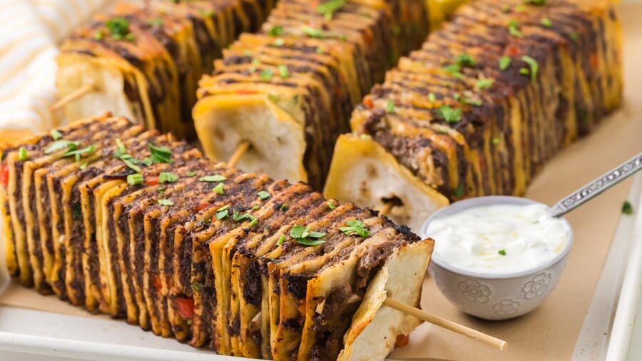 Crispy tortilla kebabs layered with seasoned beef and cheese beside creamy dipping sauce.