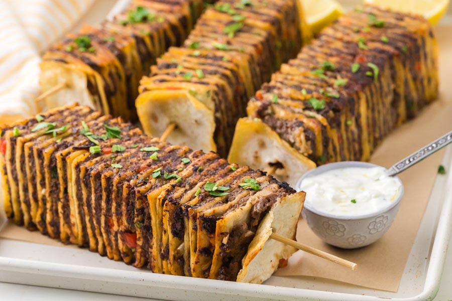 Crispy tortilla kebabs layered with seasoned beef and cheese beside creamy dipping sauce.