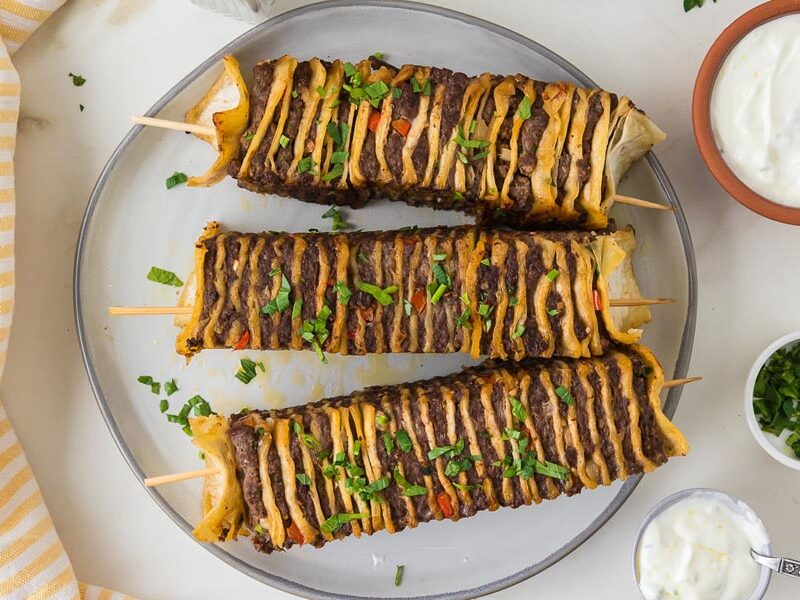 Overhead view of tortilla kebabs topped with chopped parsley and served with a creamy yogurt sauce.