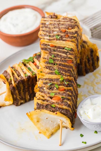 Close-up of sliced tortilla kebabs layered with seasoned beef and tortillas served with creamy sauce on the side.