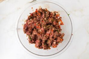 Seasoned ground beef mixture with herbs and diced peppers prepared in a glass mixing bowl.