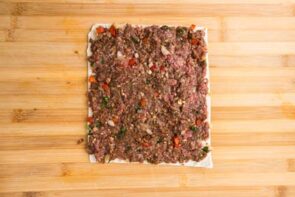 Seasoned beef mixture spread evenly over a tortilla rectangle on a cutting board.