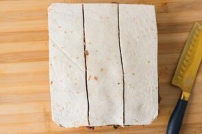 Large stacked tortilla kebab slab sliced into long strips on a cutting board.