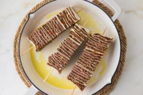 Raw tortilla kebabs threaded onto skewers and placed in an oiled baking dish before cooking.