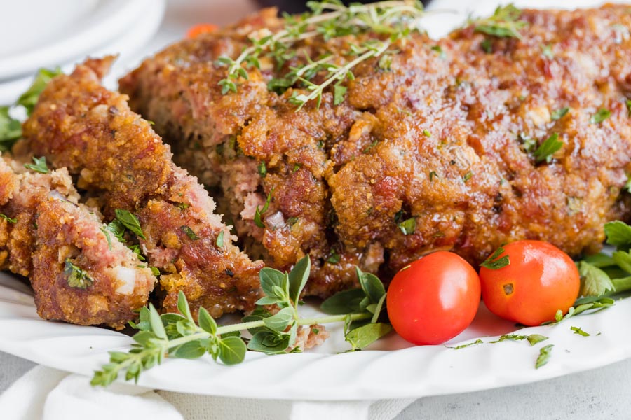 closeup of juicy meatloaf with fresh herbs around