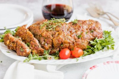 juicy meatloaf on a plate with herbs and tomatoes