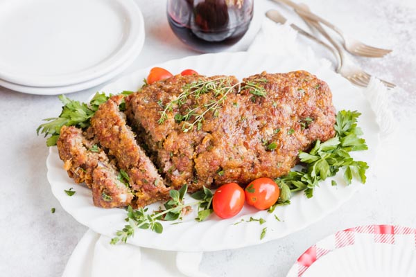 a plate of meatloaf sliced on a platter with red wine and tomatoes