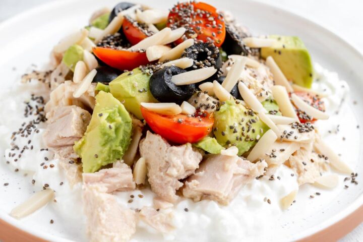 Cottage cheese bowl topped with canned tuna, avocado chunks, cherry tomatoes, olives, slivered almonds, and chia seeds.