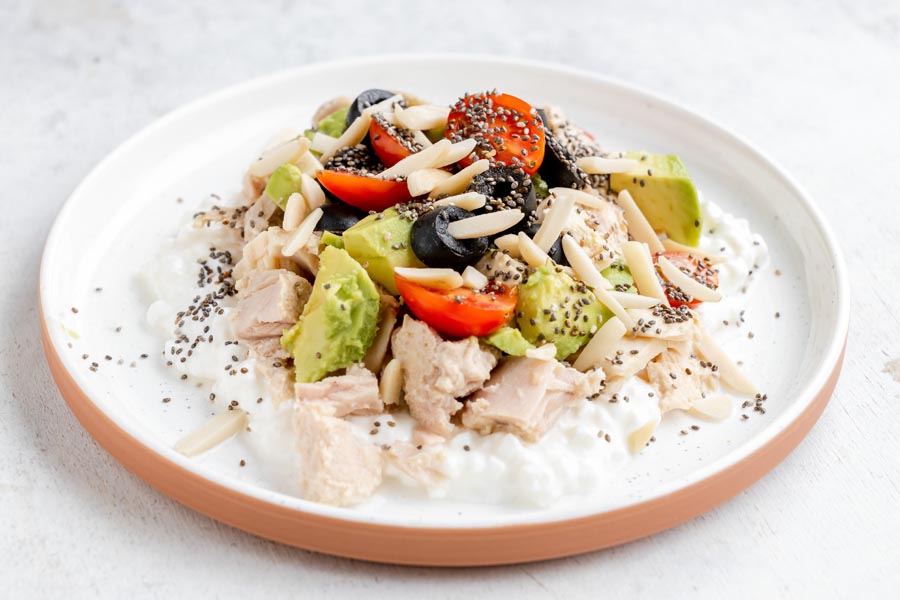 Close-up of a cottage cheese tuna bowl with avocado, cherry tomatoes, olives, and chia seeds.