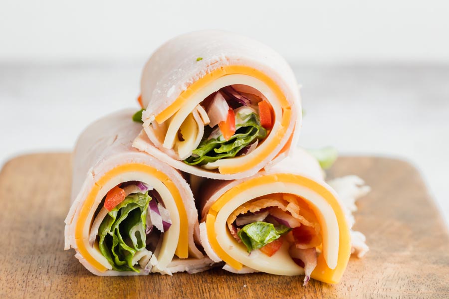 Three rolled turkey wraps on a cutting board.