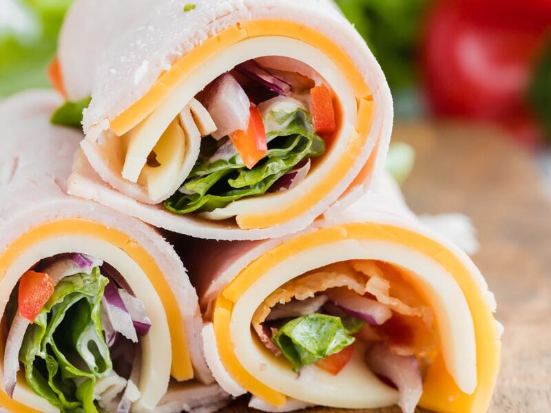 Close up of small turkey wraps made with lunch meat, cheese, lettuce, bell pepper, and mayo.