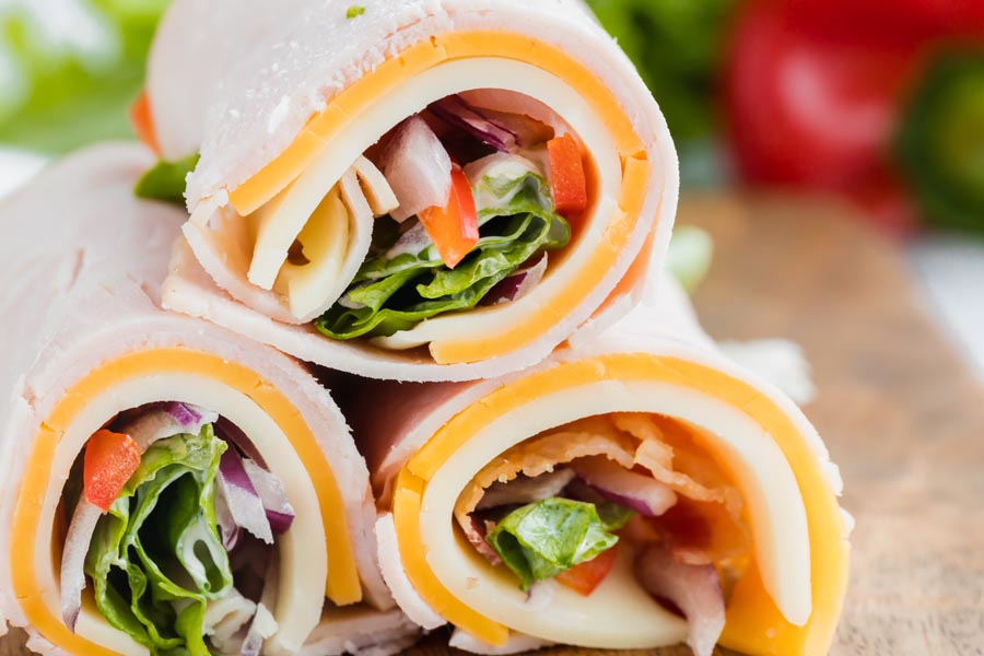 Close up of small turkey wraps made with lunch meat, cheese, lettuce, bell pepper, and mayo.