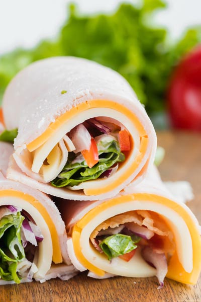 Three turkey rolls stacked on each other and filled with cheese, lettuce, bell pepper.