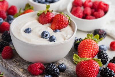 A bowl with yogurt dip inside, topped with strawberries and blueberries. Mixed berries scattered around.