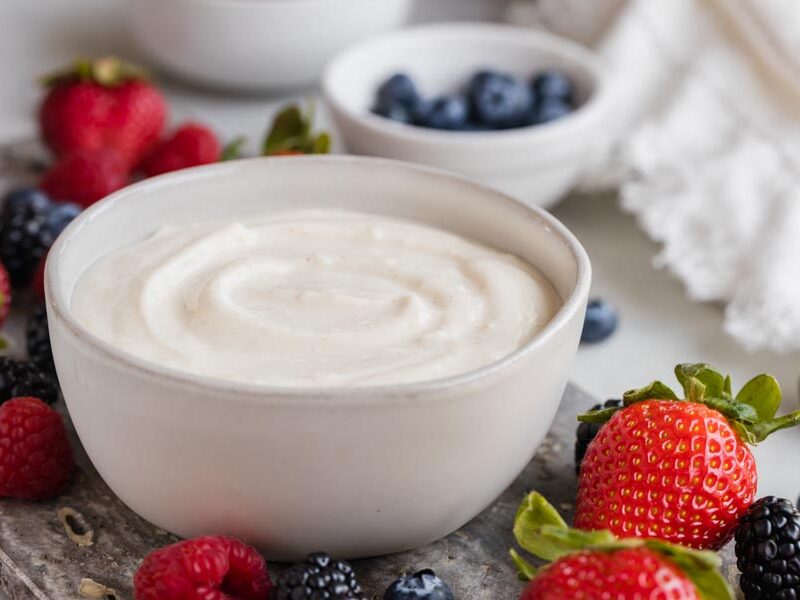 Creamy yogurt dip in a bowl with assorted berries surrounding the bowl.