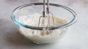 An electric mixer mixing a yogurt dip in a glass bowl.