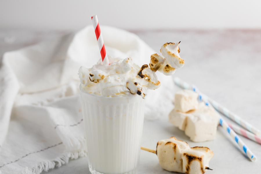 whipped cream topped milkshake in a glass with straws and marshmallows around