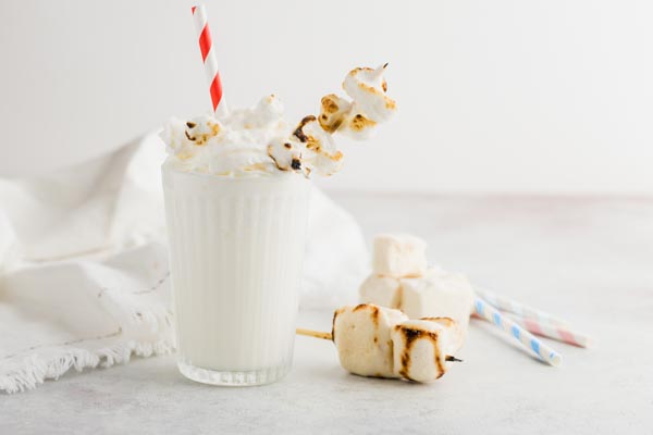 a glass with a milkshake topped with whipped cream, marshmallows and a red swirl straw