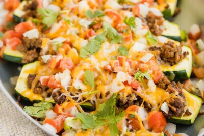 cheesy taco meat stuffed into a zucchinis on a skillet and topped with pico de gallo.