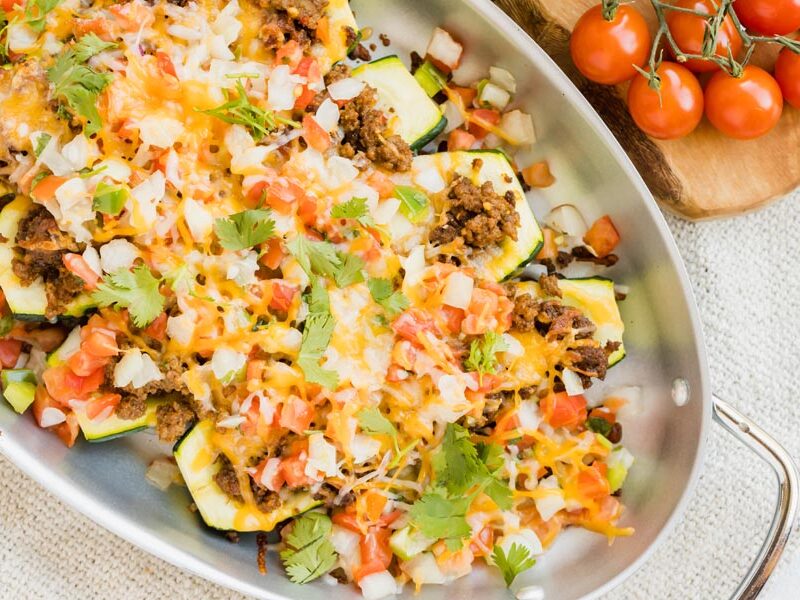 Stuffed zucchini lined in a skillet topped with pico de gallo, seasoned beef and cilantro.
