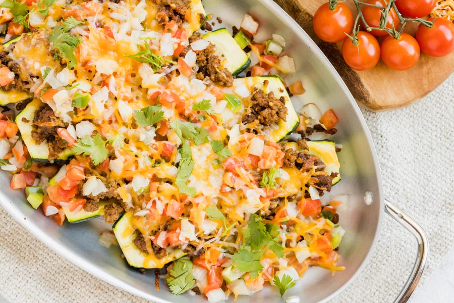 Stuffed zucchini lined in a skillet topped with pico de gallo, seasoned beef and cilantro.