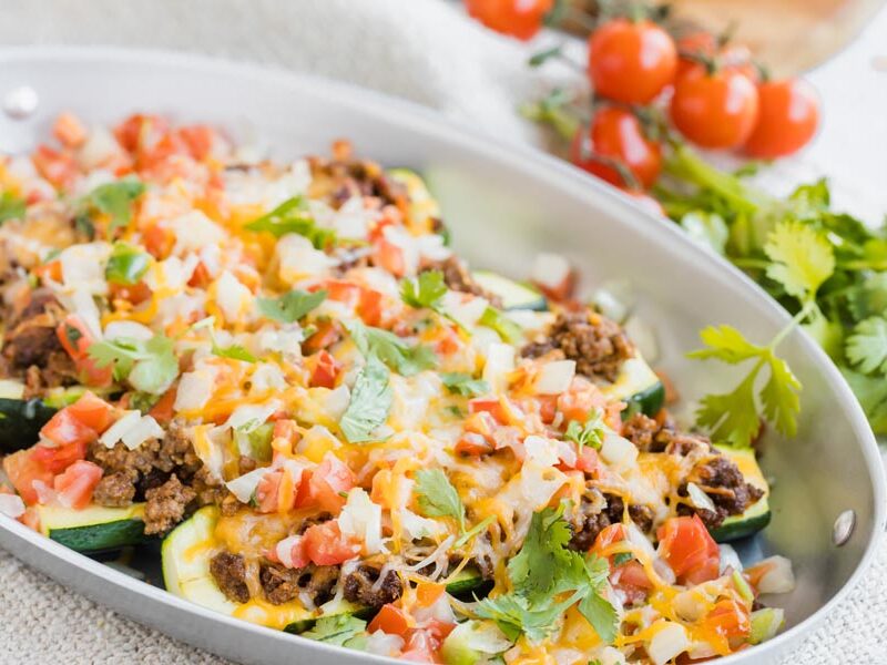 Melted cheese on top of taco stuffed zucchinis in a skillet.