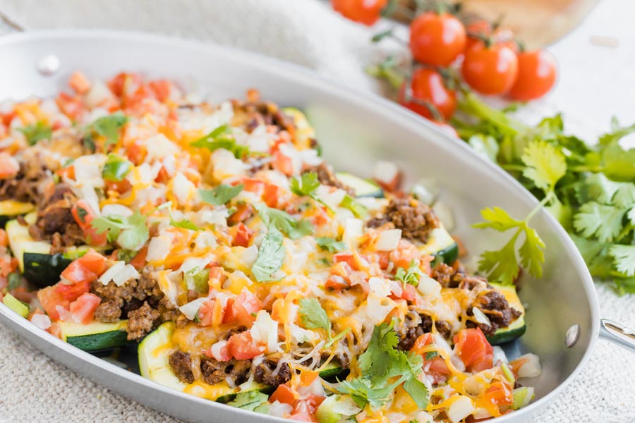 Melted cheese on top of taco stuffed zucchinis in a skillet.