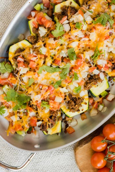 Taco toppings scattered all over ground beef stuffed zucchini boats.