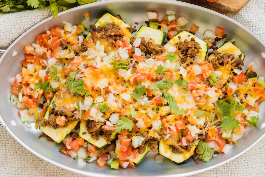 A skillet filled with zucchini boats topped with taco meat, cheese and pico de gallo.